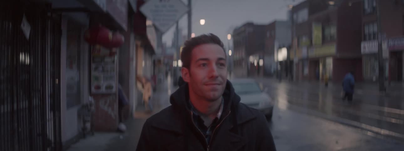A man smiles while walking on a city sidewalk on a rainy night