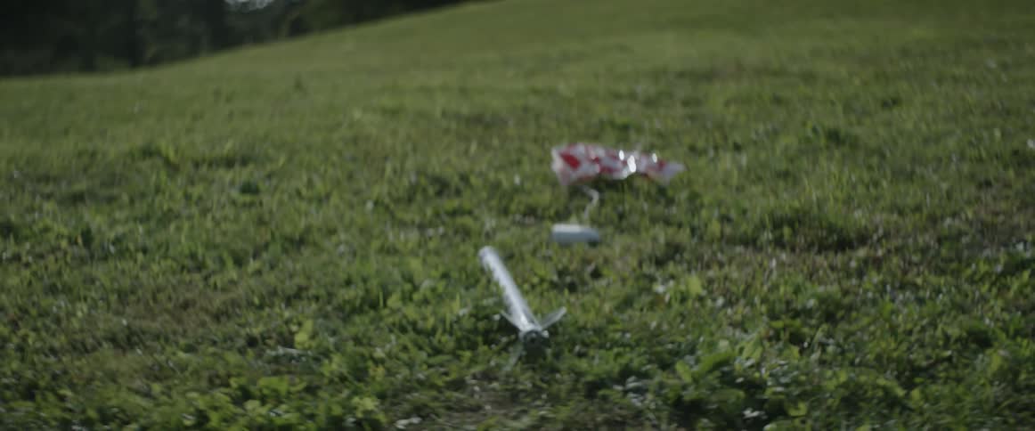 A toy rocket parachutes from the sky to the grass