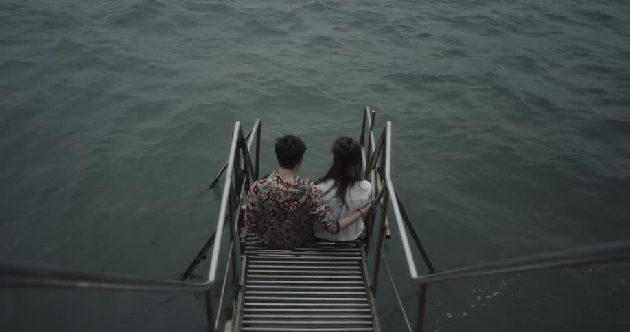 A man and woman sit at the end of a dock