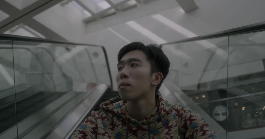A man looks around as he sits riding an escalator down
