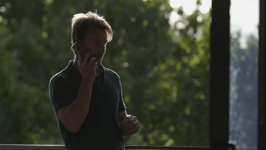 A man talks on his phone on his balcony