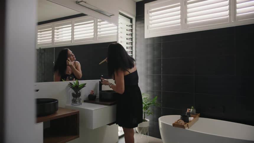 A woman in black applies makeup at a large mirror