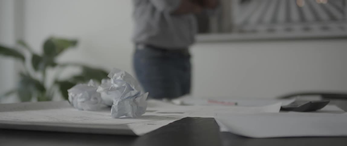 Person paces behind a desk with crumpled paper balls on it