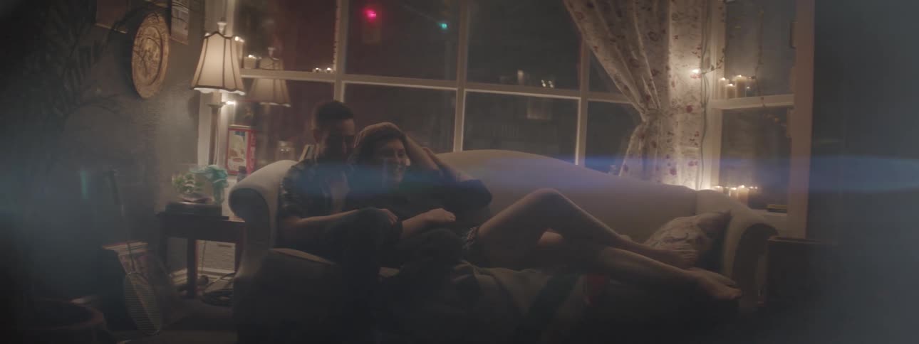 A man and woman sit on the couch laughing
