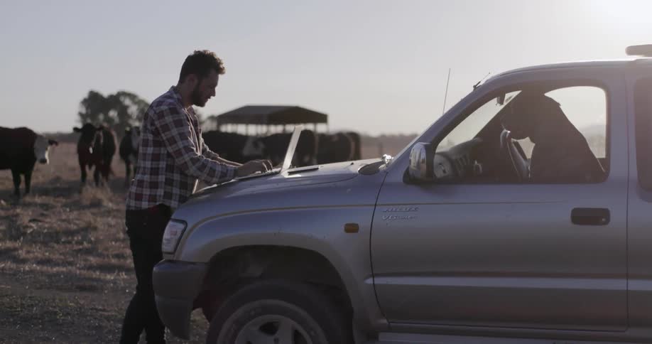 A man types on a laptop sitting on truck hood while on a ranch