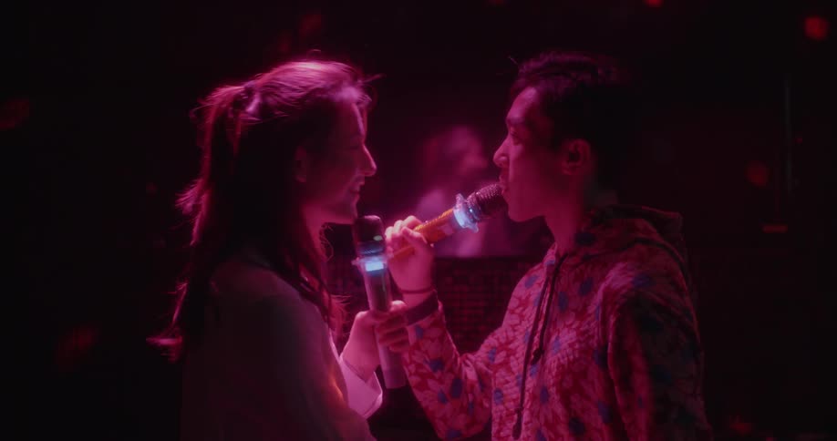 A man and woman look at each other as they sing into microphones