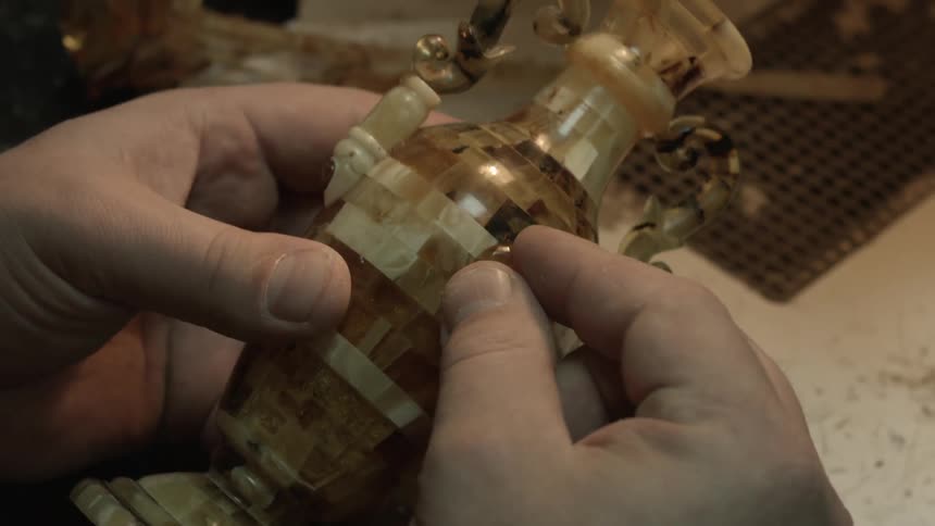 A man glues a yellow gem to a vase