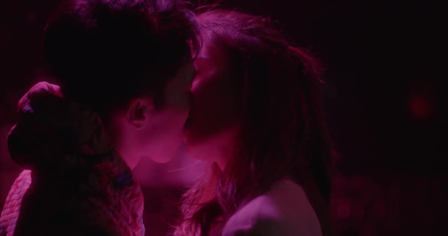 Man and woman illuminated by purple light talk and kiss