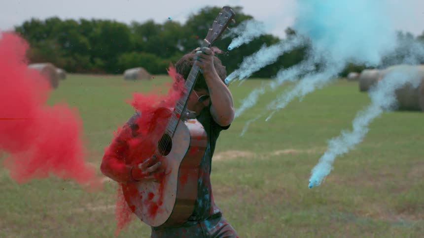 A man plays guitar as colored dirt hits him