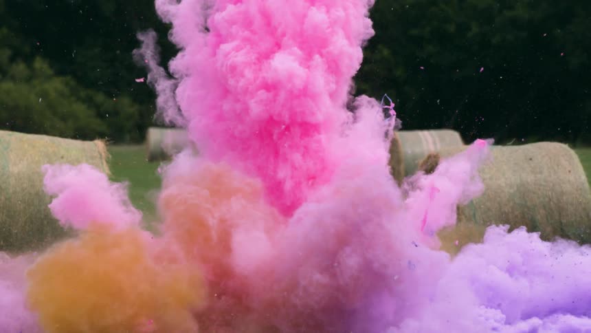 Colored smoke explodes in a field with hay bales