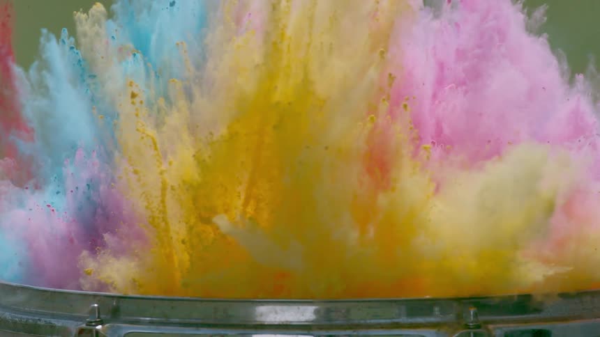 Drumsticks hit a drum causing colored powder to explode into the air