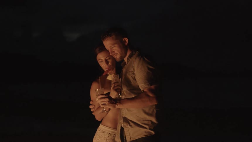 Man and woman hug and hold drinks in firelight