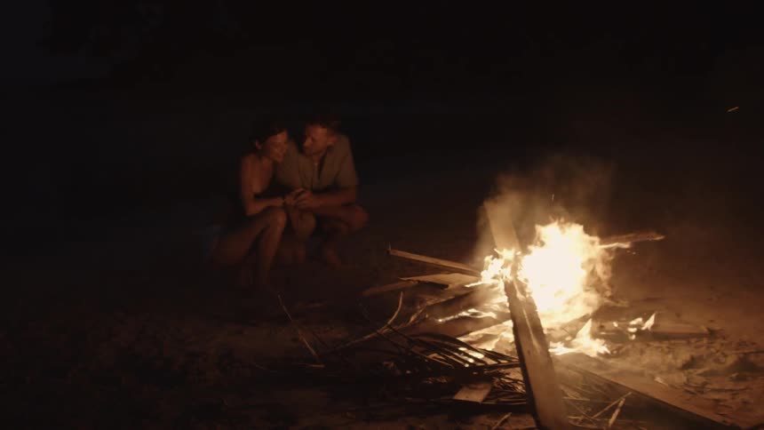A man and woman sit next to a bonfire