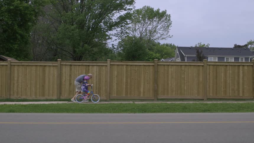 Man helping little girl to learn to ride bike on neighborhood sidewalk