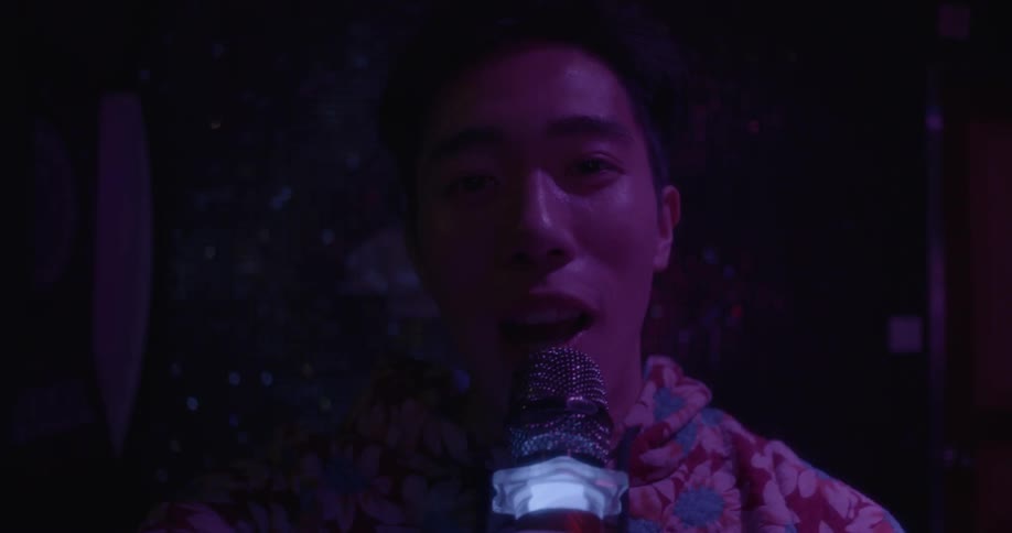 A man is singing into a microphone in the dark