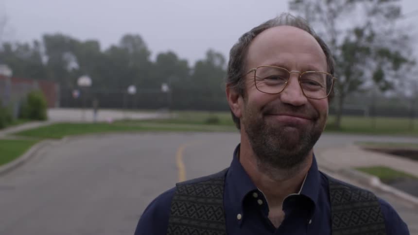 A man wearing glasses stands in the street