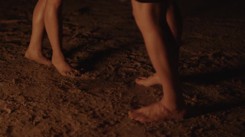 Two barefoot people dancing in firelight on a beach