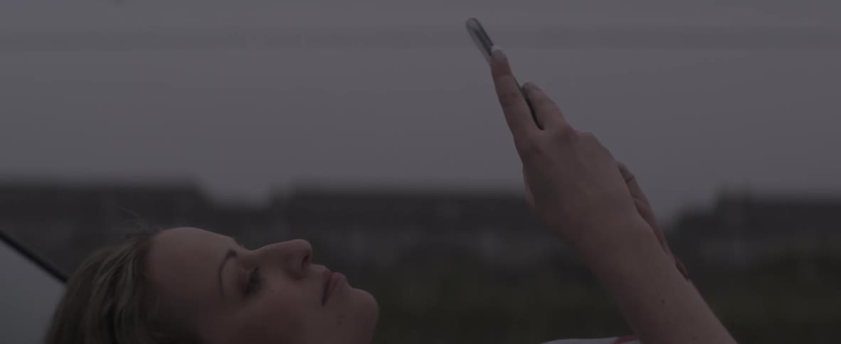 A woman lays in the grass checking her phone