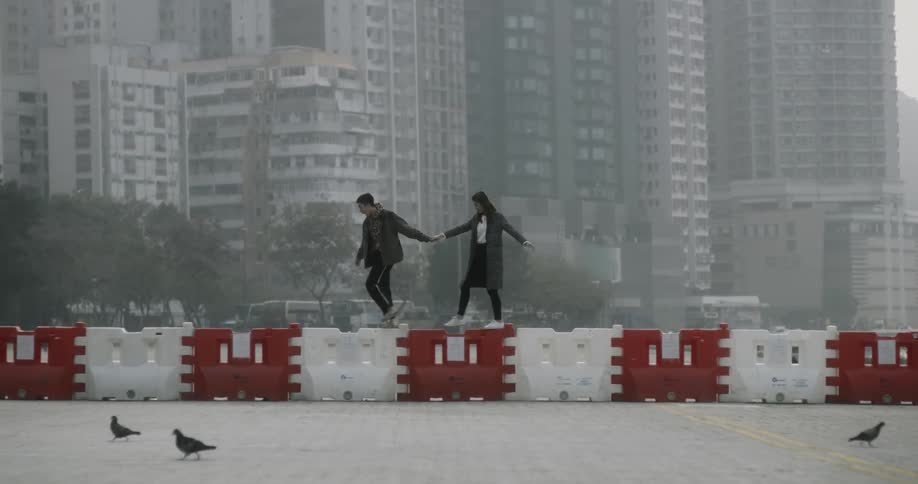 A man and woman balance walking over some blocks near a city