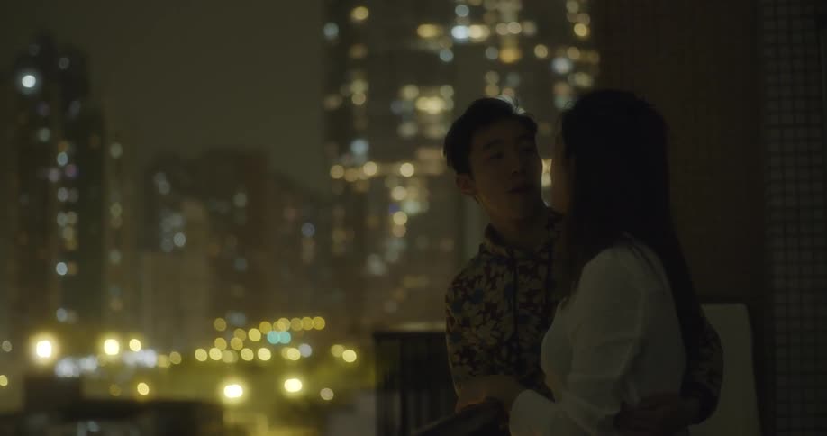 A man and woman kiss overlooking a city at night