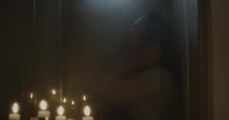 A woman is sitting fully clothed showering in a dark bathroom