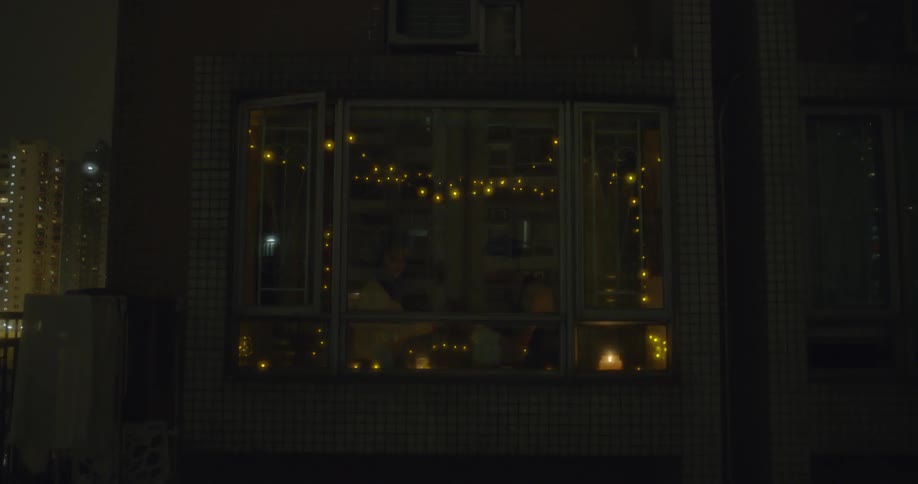 A woman lights a red candle near a window