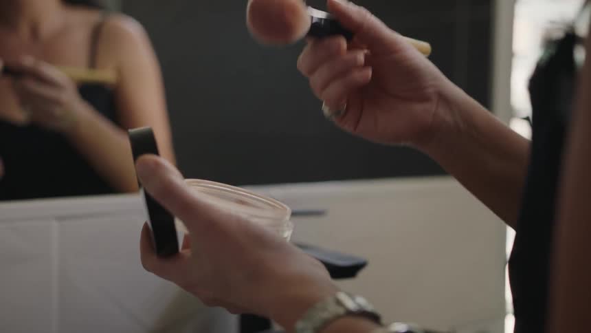 A woman applies face powder with a makeup brush