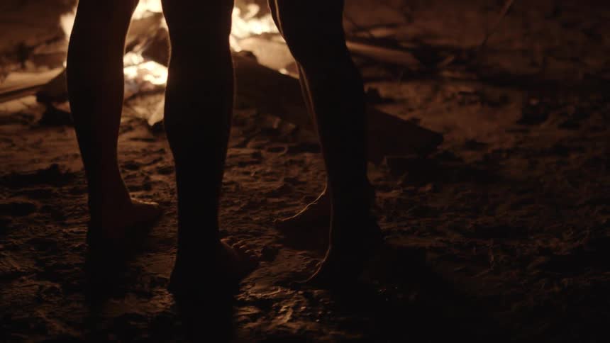 A man and woman stand next to a bonfire on the beach