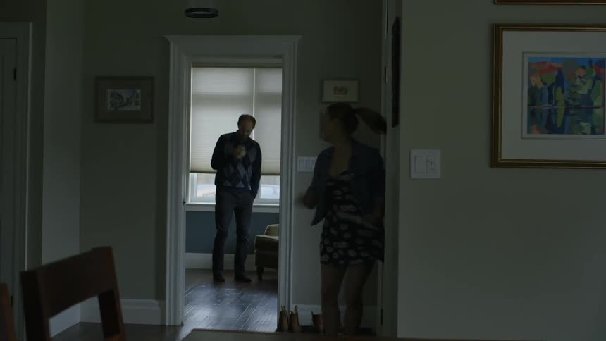 A man is pacing in the room ahead as a woman runs in the house