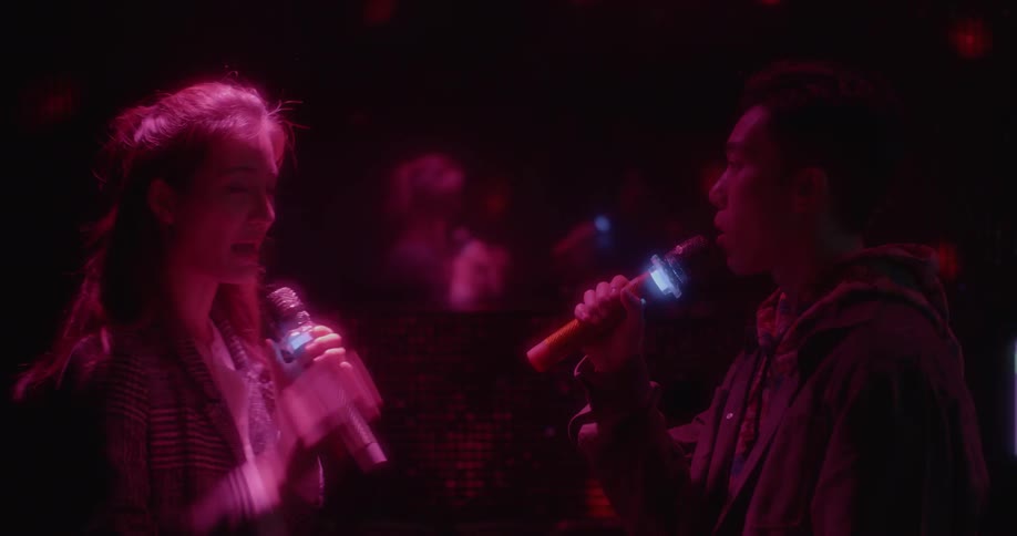 A man and woman sing karaoke in a dark room with red lights