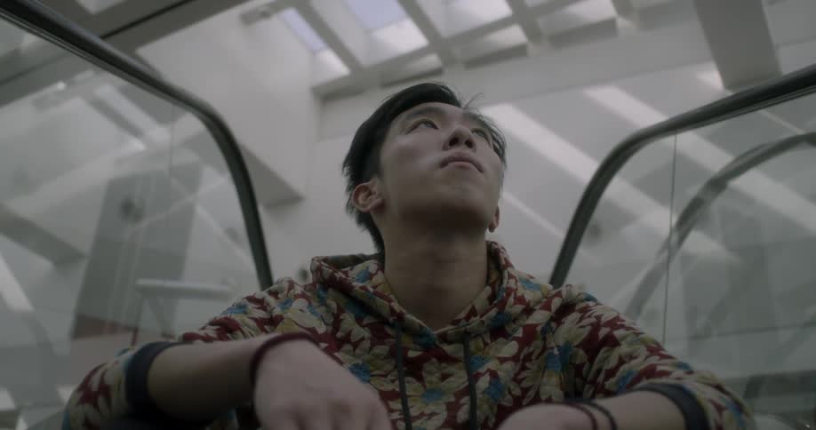 A man sits on a moving escalator and looks up at the ceiling