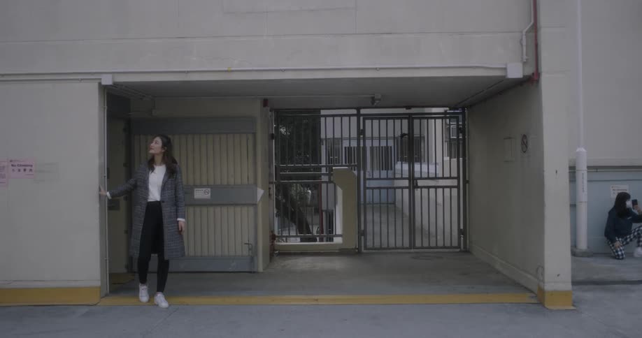 A woman exits a building and looks towards the sky