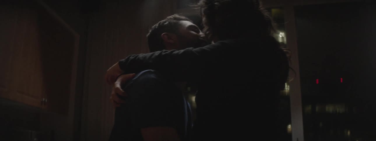 A man and woman hug and kiss each other in the dark room