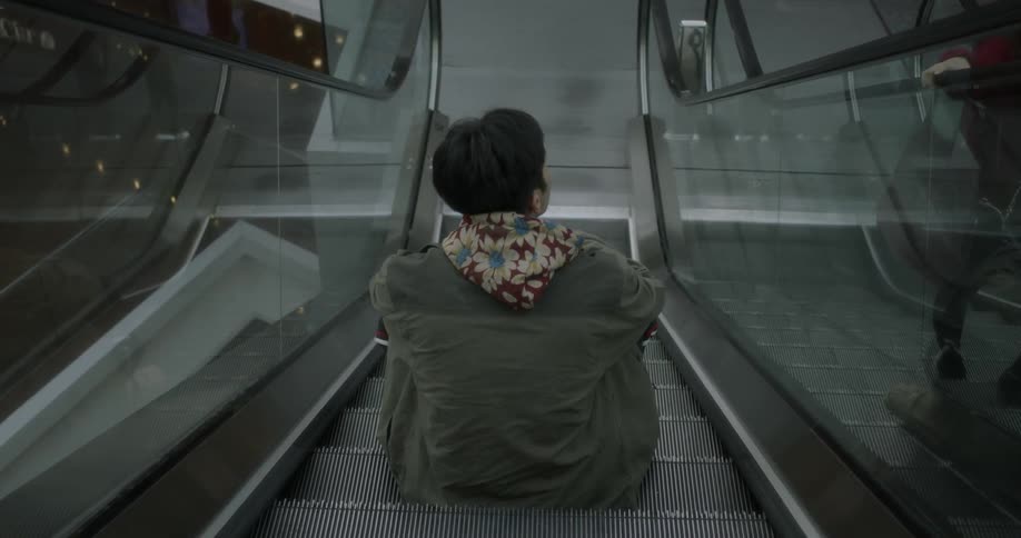 A man with a hood is sitting on the escalator