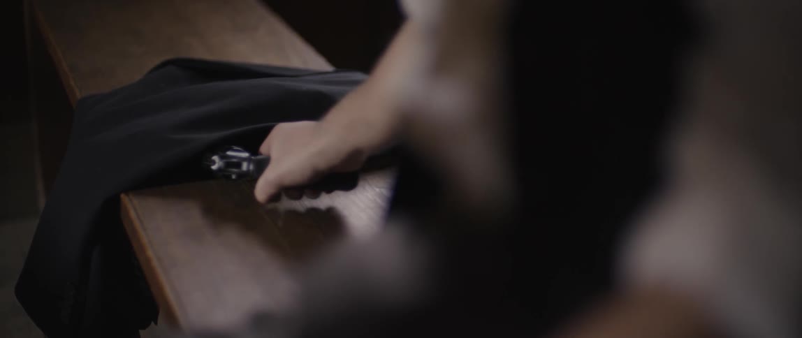 A man pulls a gun from beneath a jacket while sitting on a bench