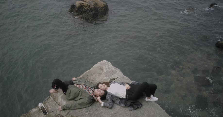 Man and woman laying next to each other on rock next to body of water