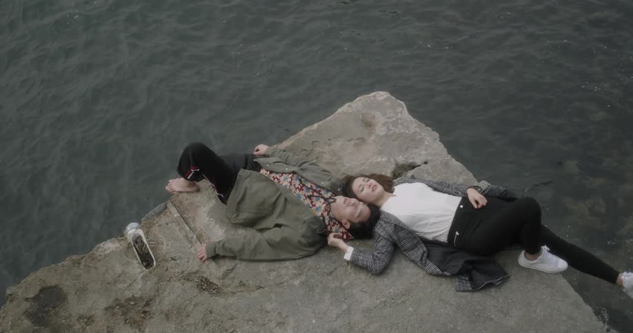 A man and woman lay down head to head by the water