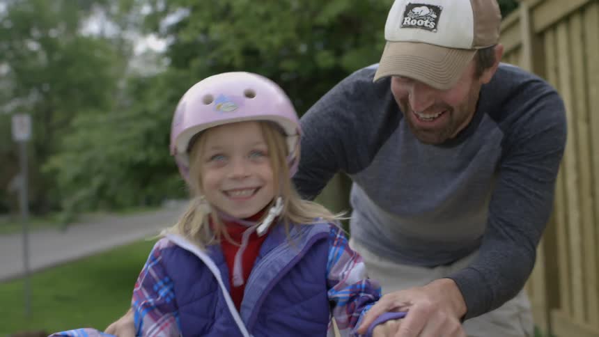 A child smiles as her parent helps her ride a bicycle