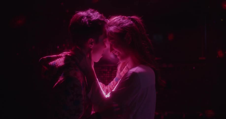 A man and woman hold each other with red light on them