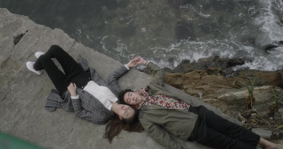 Man and woman laying next to each other on rock with ocean waves below