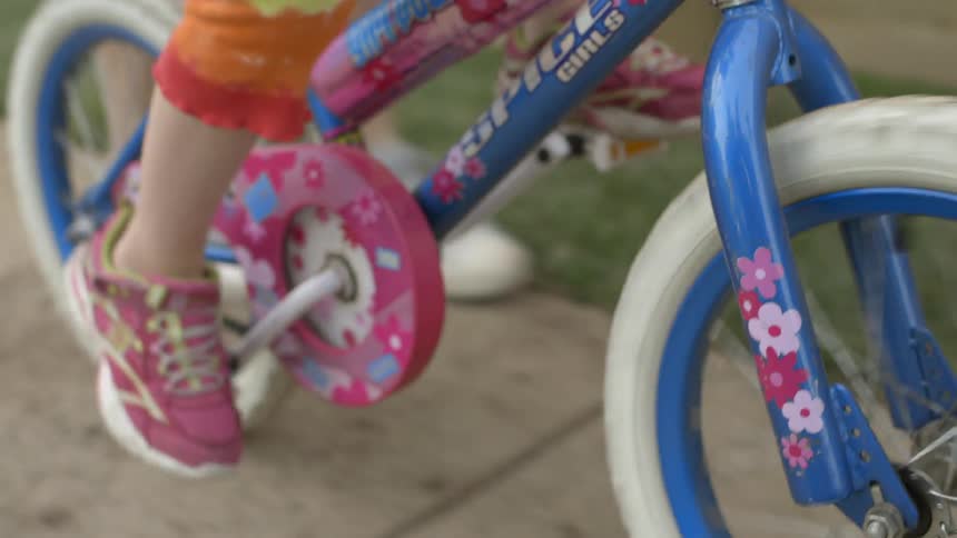 A girl pedals a bike while a person walks alongside
