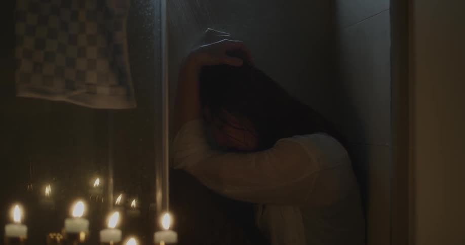 A woman sits in the shower fully clothed