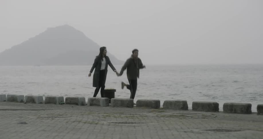 A man and woman hold hands and run along the pier