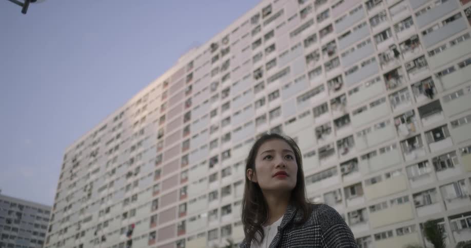 A woman stands in front of a large apartment building