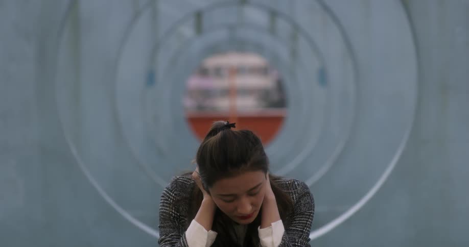 A woman sitting outside holds her head and looks down