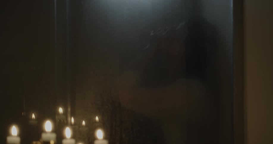 A woman is in the shower in this dark bathroom with some candles