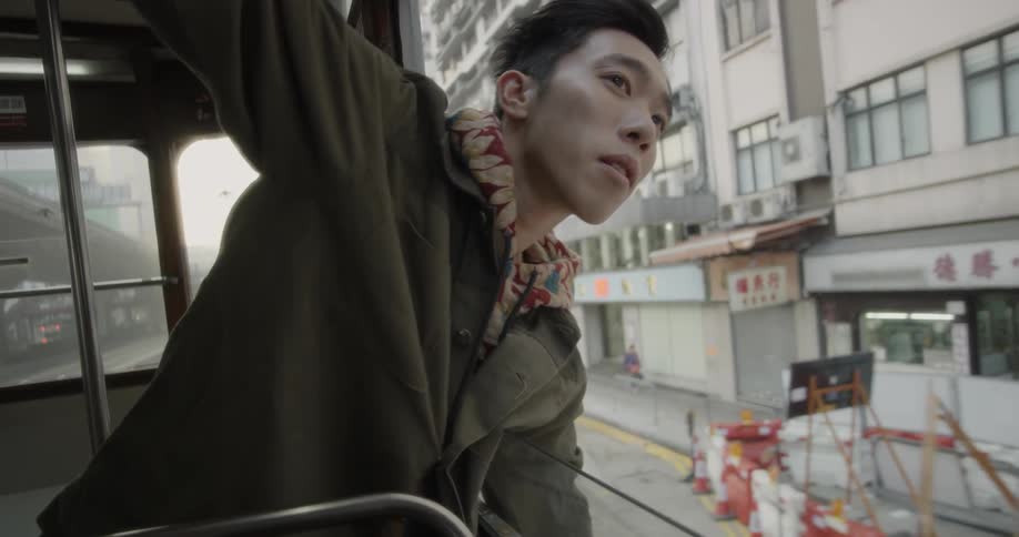 A man is hanging out of a bus looking at the buildings as he passes