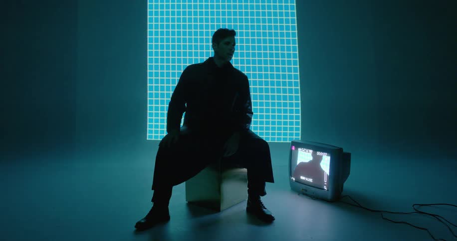 A man is sitting down in front of a television displaying him