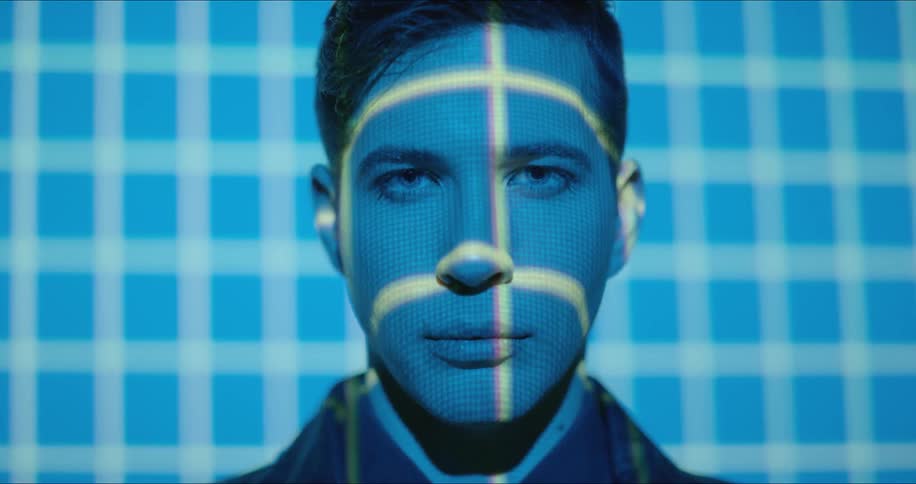 A man looks forward blinking as lights flash on his face