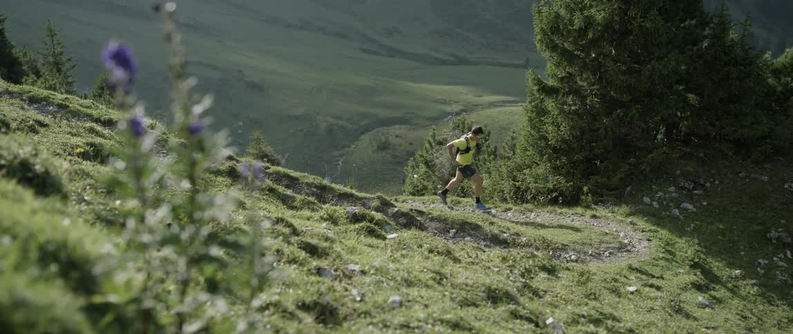 Man jogs up a grassy mountain on a sunny day